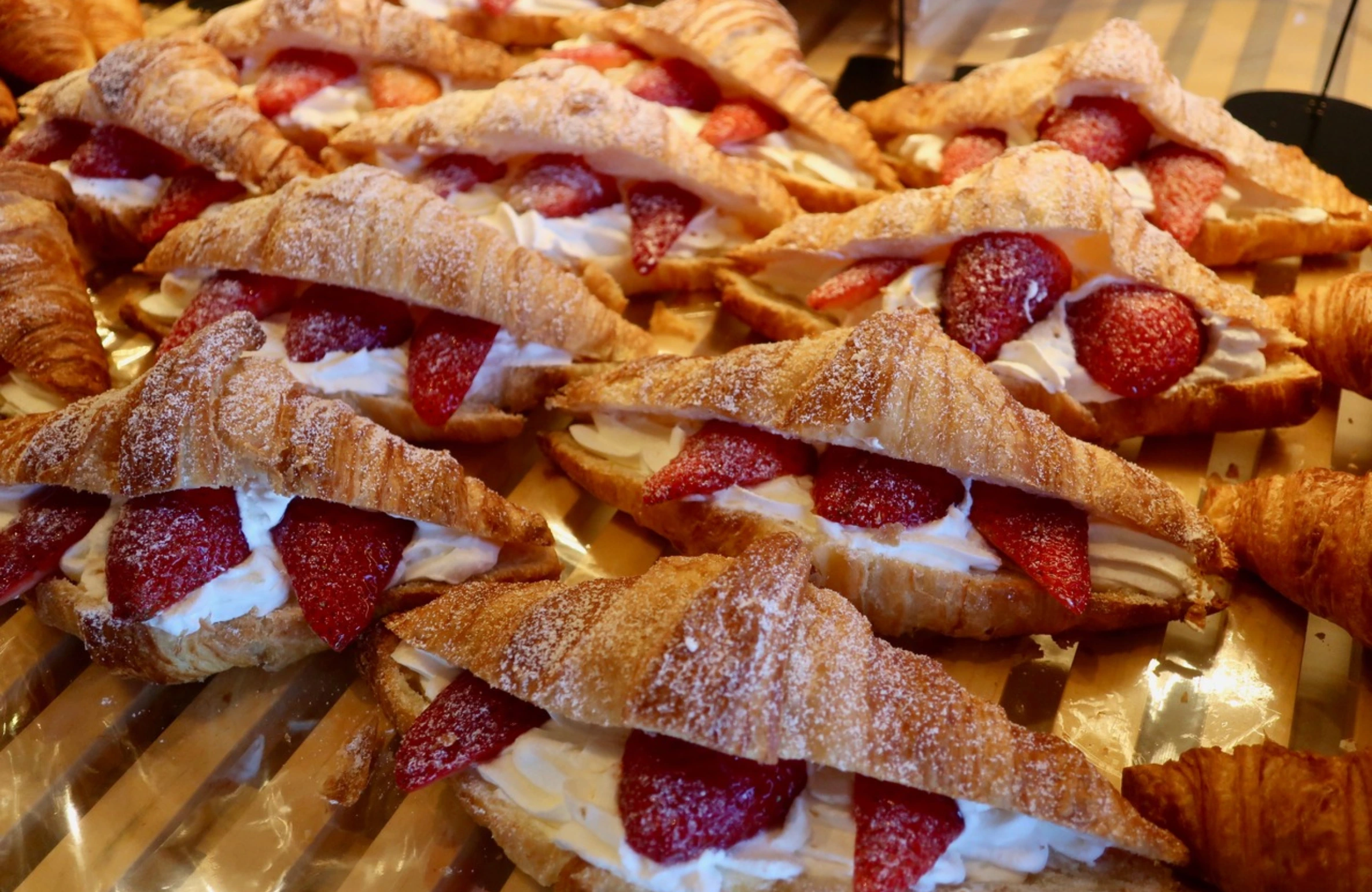 Freshly baked croissants filled with whipped cream and strawberries, dusted with sugar — Why Our Croissants Are Different.