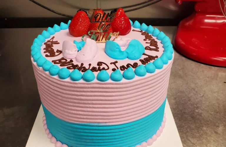 Beautiful custom cake with pink and blue frosting, decorated with chocolate drizzle and fresh strawberries on top. Example of a stunning custom cake design made in Des Moines by TOUS les JOURS.