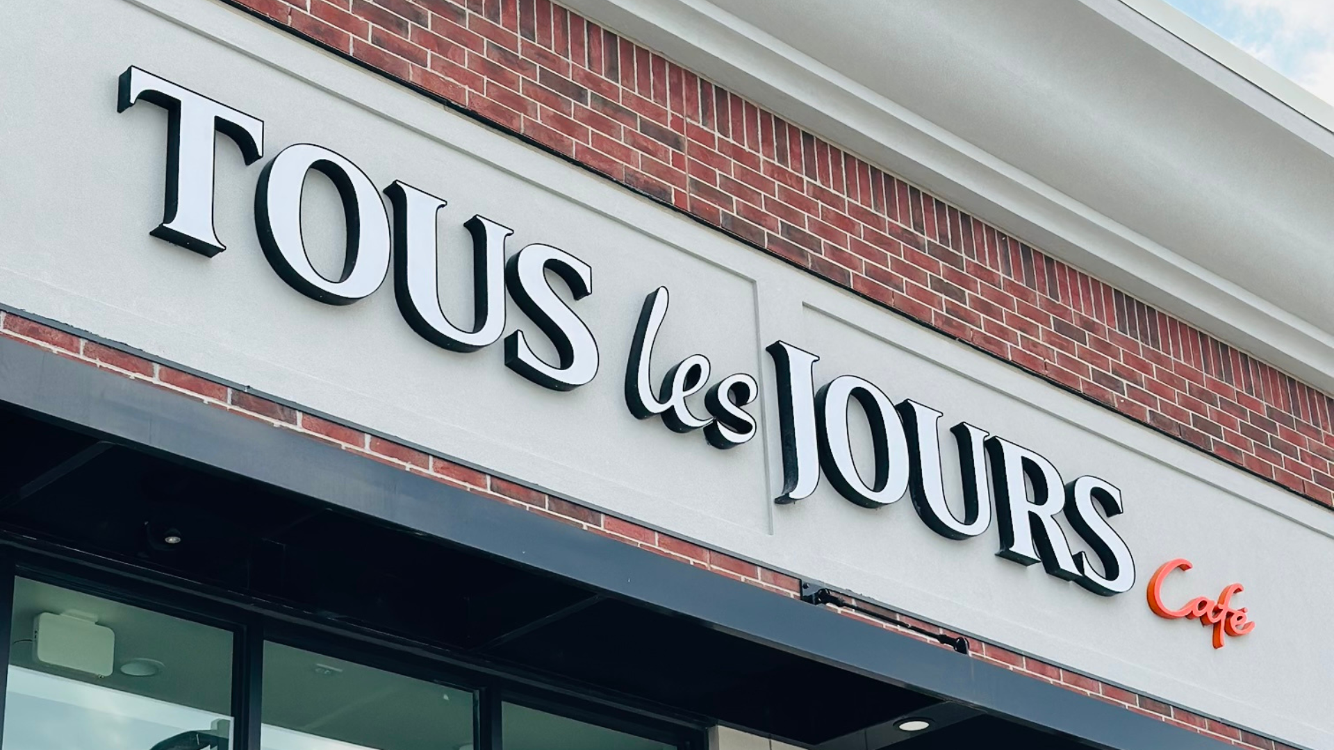 Exterior storefront sign of TOUS les JOURS Café in Iowa, a neighborhood favorite and winner of the Best of the West Award.
